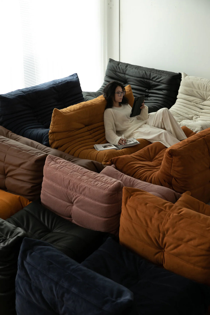 Lady sitting on a colorful modern sofa with cushions, reading a book.