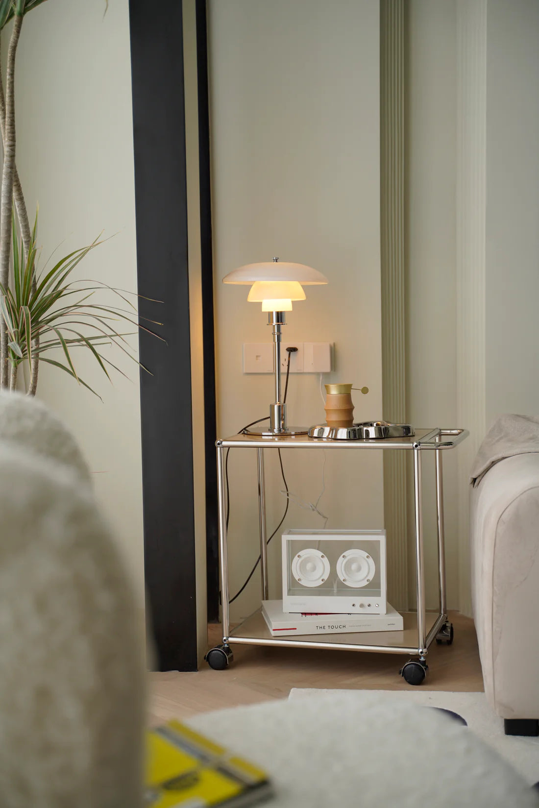 Modern interior with a inspired recreation USM modular glass side table holding a lamp and decorative items.