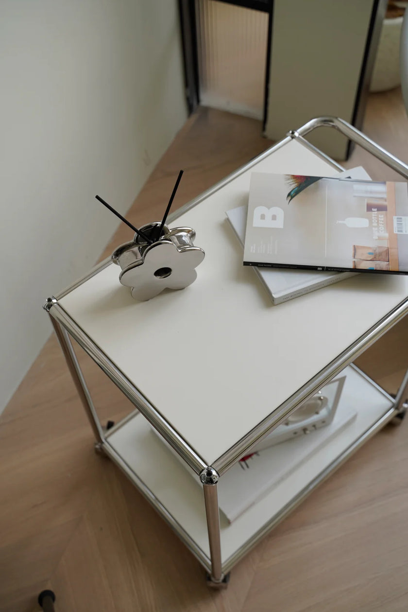 Inspired recreation USM modular small white side table or handcart with a metal frame on a wooden floor, featuring a decorative item and books
