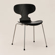 A modern black molded wood dining chair with a curved backrest and slim silver metal legs, shown against a plain light beige background.