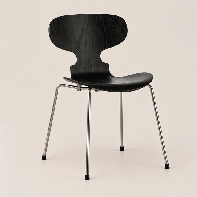 A modern black molded wood dining chair with a curved backrest and slim silver metal legs, shown against a plain light beige background.