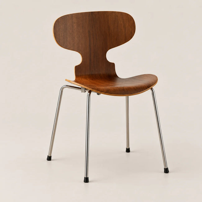 A mid-century modern wooden chair with a curved backrest and seat made of warm brown wood, supported by slim chrome metal legs with black feet, set against a plain beige background.