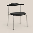 A modern dining chair with a black molded seat and curved backrest, supported by slim chrome metal legs, shown against a solid light beige background.