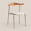 A modern dining chair with a curved light oak wood backrest, a cream upholstered seat cushion, and slim polished steel legs, shown against a solid beige background.