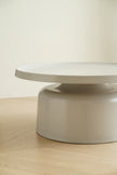 Round beige table on a light wooden floor with a plain white wall background