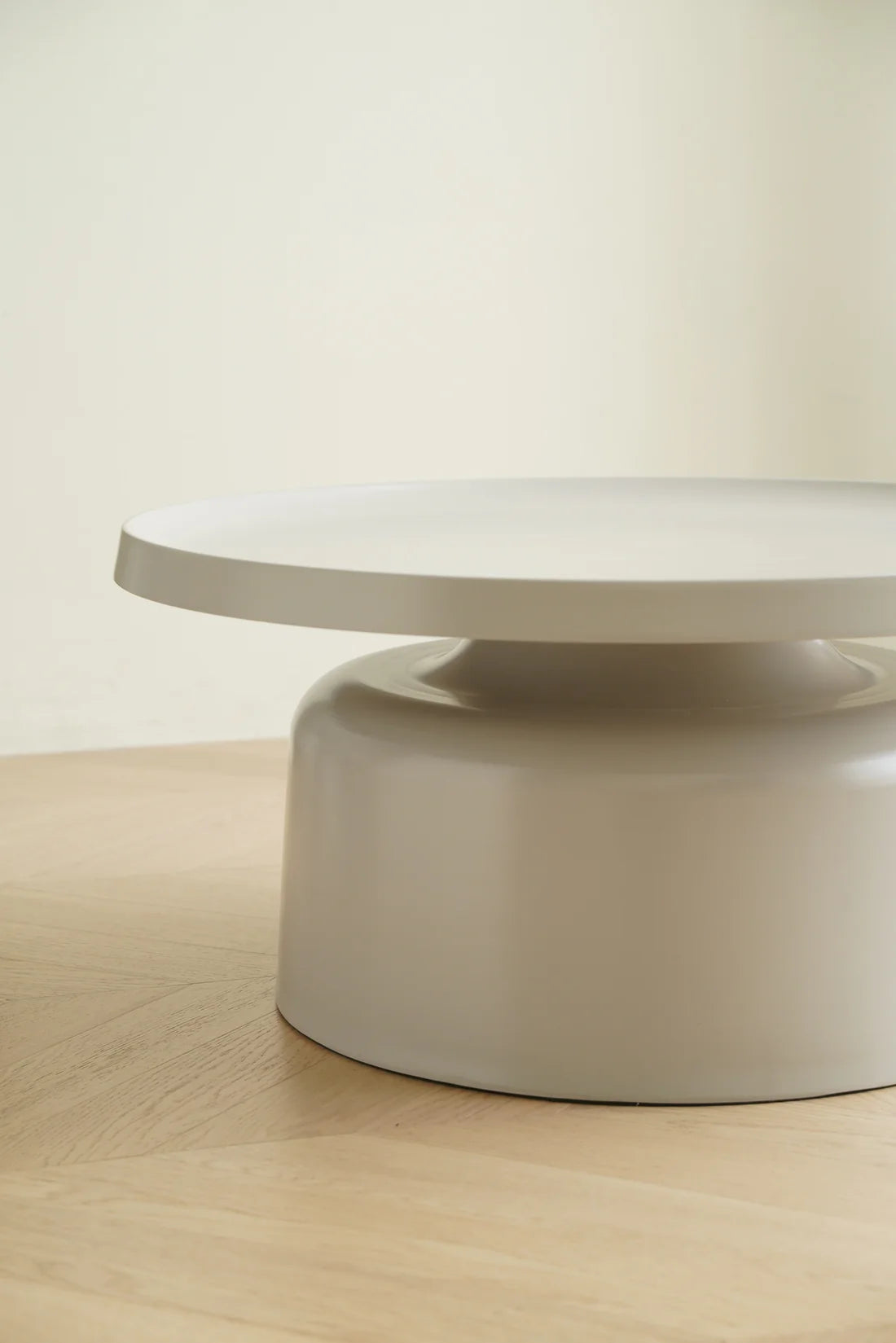 Round beige table on a light wooden floor with a plain white wall background