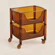 A two-tier rolling storage cart made of translucent amber-brown plastic with integrated basket-style shelves and caster wheels, shown on a plain light beige studio background.