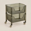 A two-tier rolling storage cart with translucent smoky gray plastic bins and a matching frame, fitted with small caster wheels, shown on a plain light beige studio background.