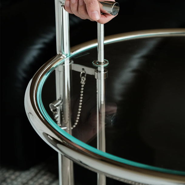 Round glass table with metal frame and handle, hand holding handle.