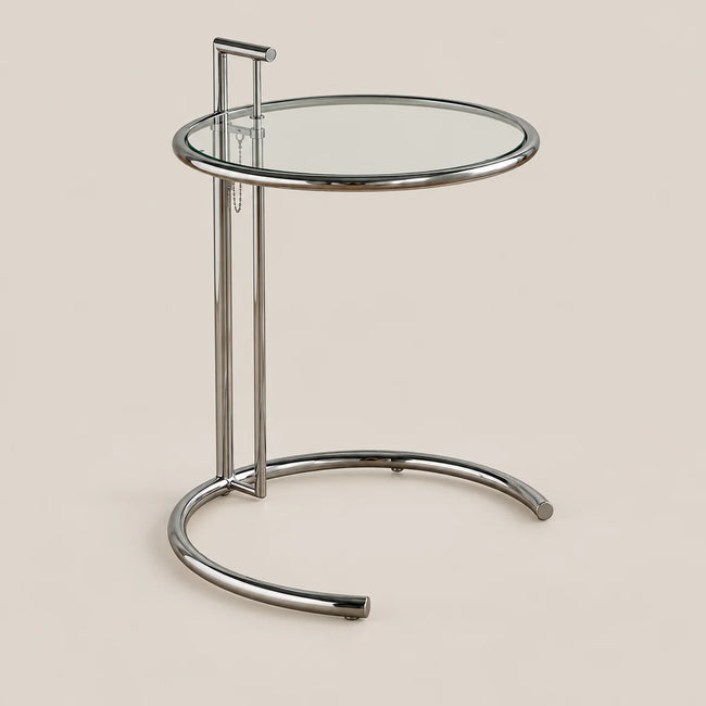 A modern round side table with a clear glass top and a polished chrome metal base, shown against a solid beige background.