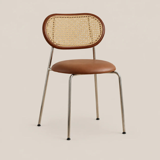A mid-century modern dining chair with a curved brown leather seat and backrest, a natural woven cane back panel, and slim chrome legs, shown against a solid beige background.