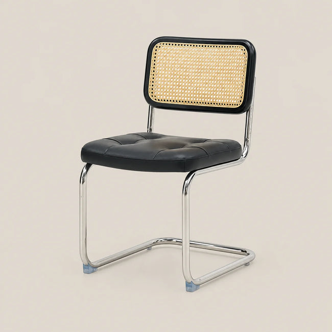 A modern dining chair with a black tufted faux-leather seat, a black-framed cane backrest, and a chrome cantilever steel base, shown against a solid beige background.