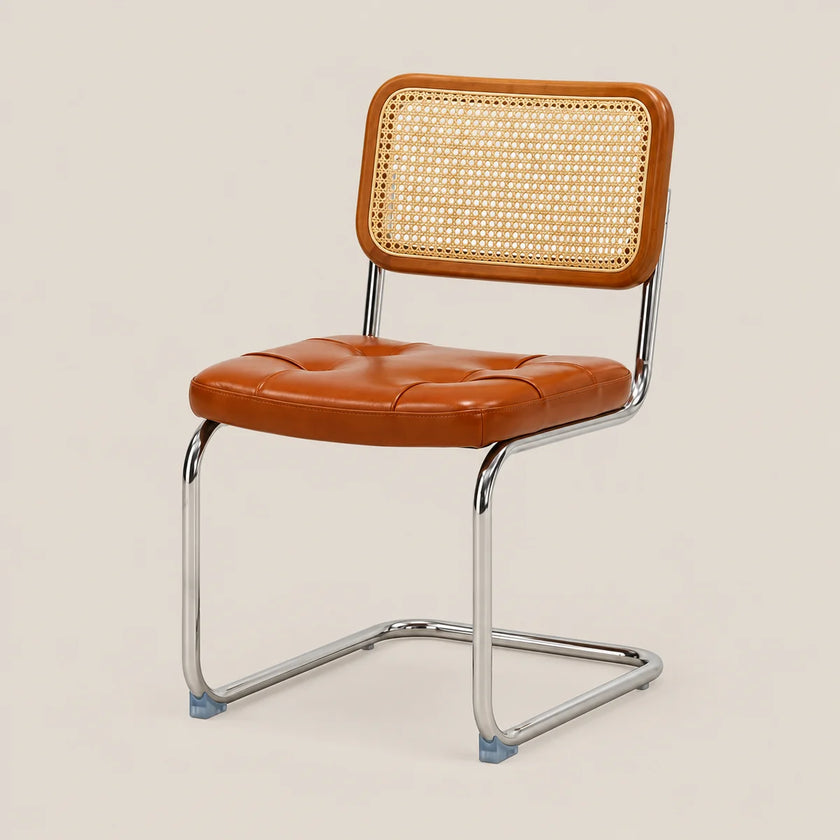 A mid-century modern side chair with a tufted cognac brown leather seat and a woven cane backrest, supported by a chrome cantilever frame on a light beige background.