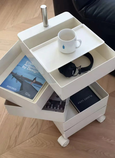 White rolling cart with books, a mug, and headphones on a wooden floor.
