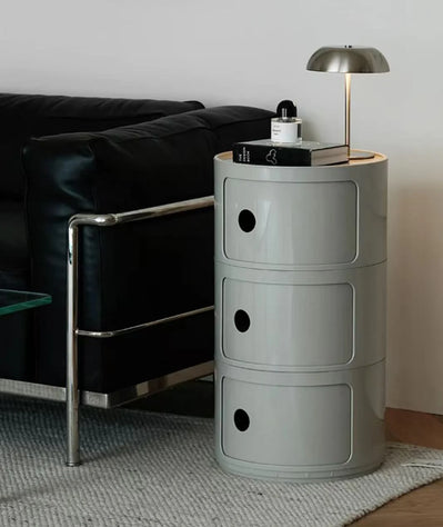 Gray cylindrical side table with three drawers in a living room setting.