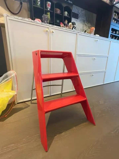 Red step stool in a kitchen setting with white cabinets and a yellow chair.