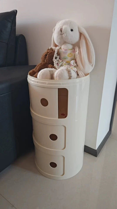 Toy storage bin with stuffed animals on a floor next to a black couch.