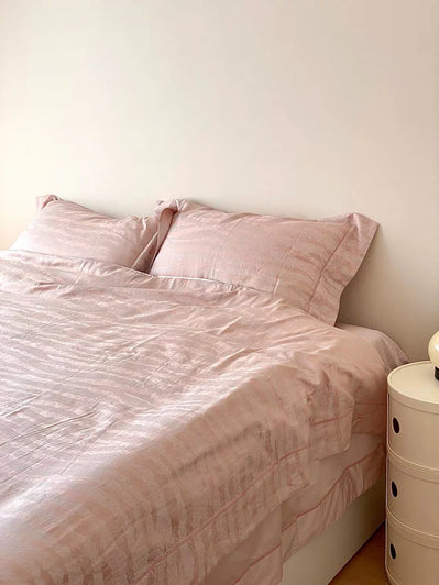 Pink bedspread and pillows on a bed against a white wall.