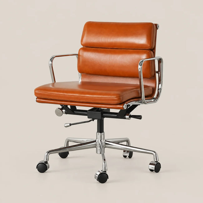 A mid-century modern office chair with a warm cognac brown leather seat and backrest, supported by a chrome-finished metal frame and five black caster wheels, set against a solid light beige background.