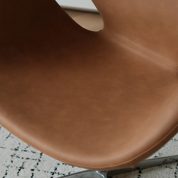 Close-up of a brown leather chair seat on a patterned floor.