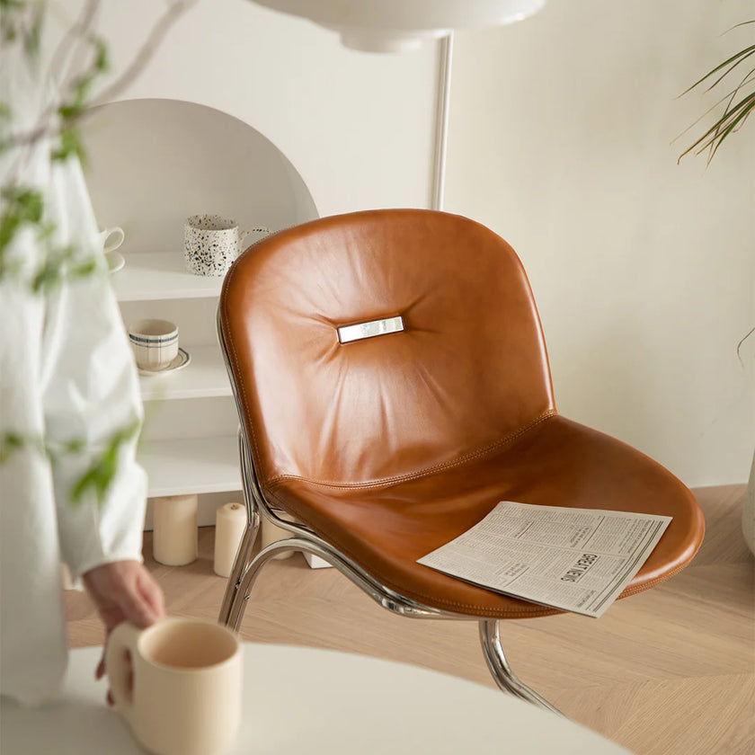 Brown leather chair with a newspaper on it in a room with a person holding a mug.