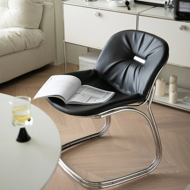 Modern black chair with a magazine on a wooden floor in a living room setting.