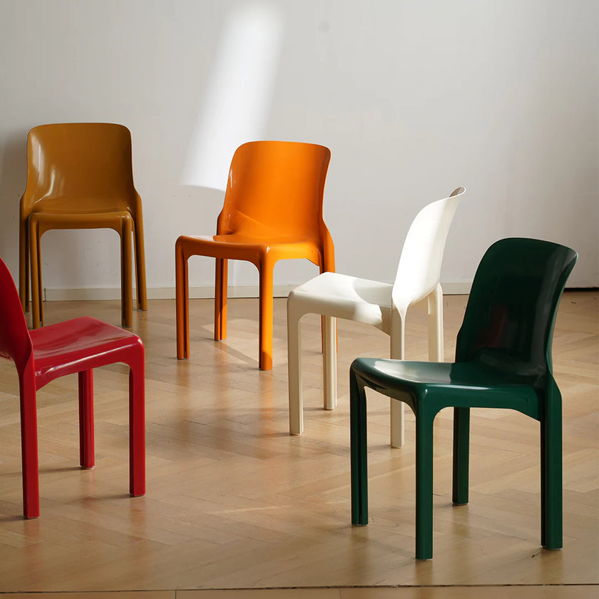 Five colorful chairs (red, orange, white, green) arranged on a wooden floor with a white wall background.