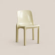A glossy molded plastic dining chair in a pale cream or light beige color, shown from a three-quarter angle against a solid, warm beige background.