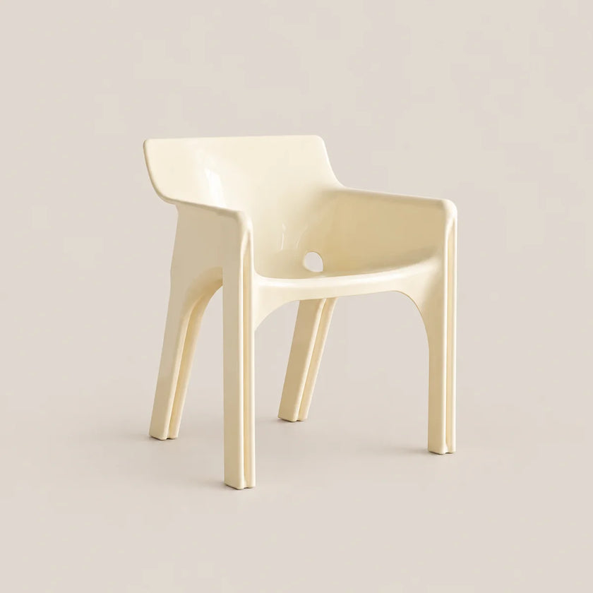 A modern molded plastic armchair in a glossy cream color, set against a solid, warm off-white background.