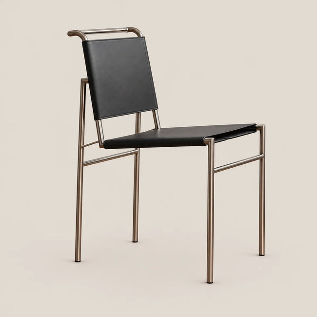 A modern dining chair with a black leather seat and backrest, supported by a slim bronze-finished metal frame, shown against a solid light beige background.