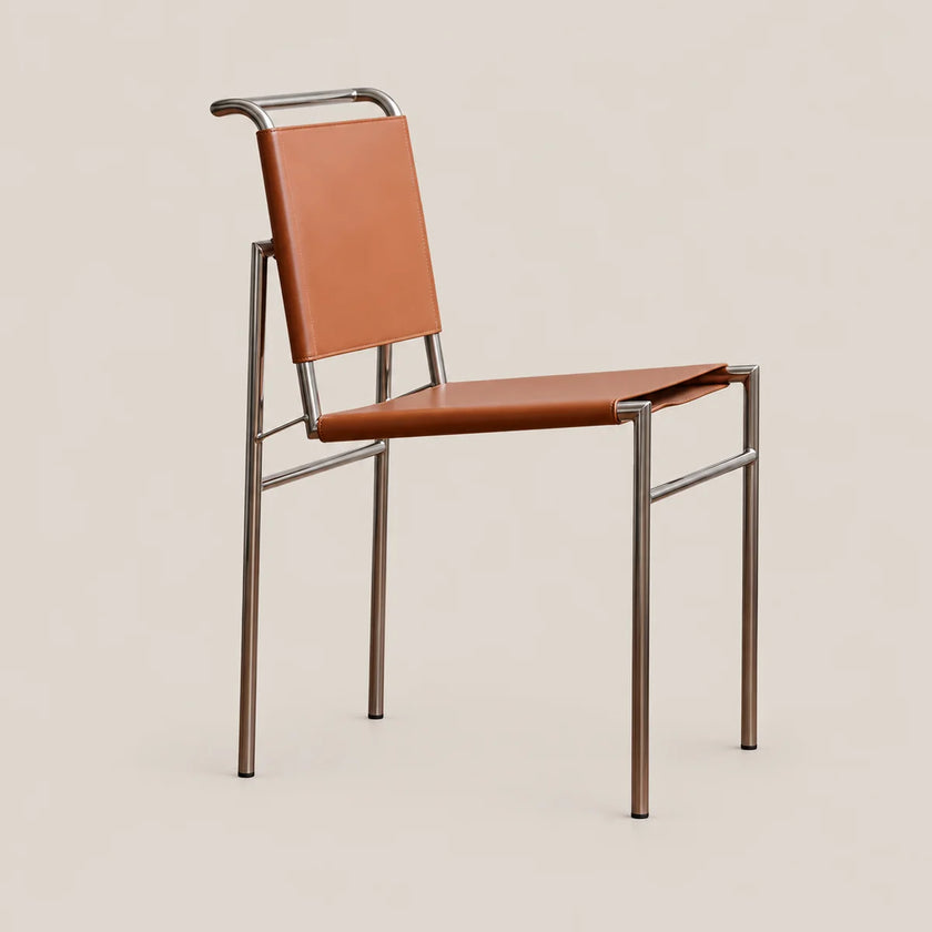 A modern mid-century style chair with a warm brown leather seat and backrest, supported by a slim brushed metal frame, shown against a solid beige background.