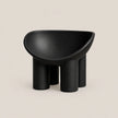 A minimalist black molded stool with a rounded, bowl-like seat and four cylindrical legs, shown against a solid light beige background.