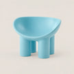 A light blue molded plastic stool with a rounded, bowl-like seat and four cylindrical legs, shown on a plain beige background.
