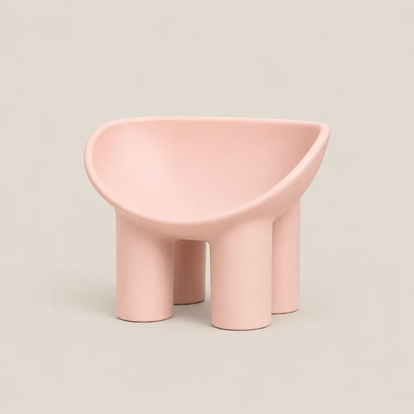 A modern, minimalist four-legged stool in a soft pastel pink color, set against a solid light beige background.