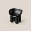 A minimalist black molded stool with a rounded, bowl-like seat and four cylindrical legs, set against a solid light beige background.