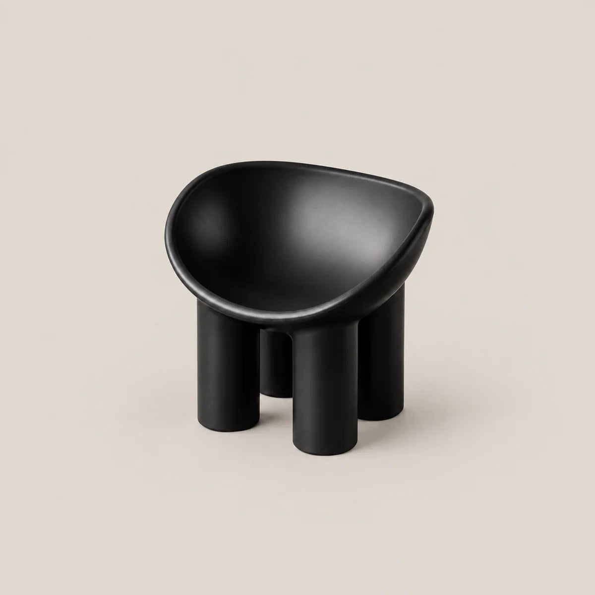 A minimalist black molded stool with a rounded, bowl-like seat and four cylindrical legs, set against a solid light beige background.