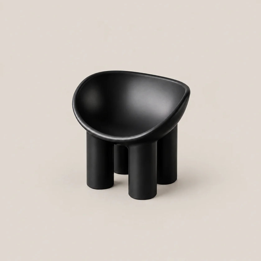 A minimalist black molded stool with a rounded, bowl-like seat and four cylindrical legs, set against a solid light beige background.