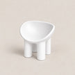A minimalist white molded chair with a rounded, bowl-like seat and four cylindrical legs, set against a solid beige background.
