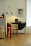 Small home office with a black wall-mounted desk, red chair, and framed picture on a white wall.