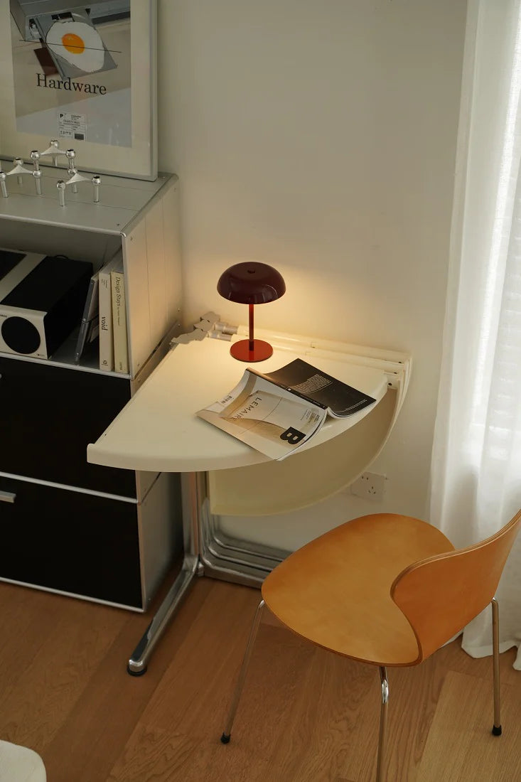 Small folding table with a lamp and magazine next to a wooden chair in a room.