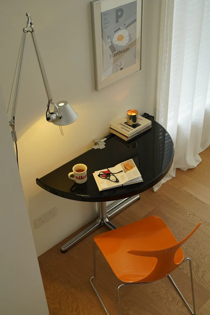 Small round black table with a lamp, cup, and book next to an orange chair in a room.
