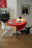 Modern interior with a red round table, white chair, and black chair against a wall with a framed picture.