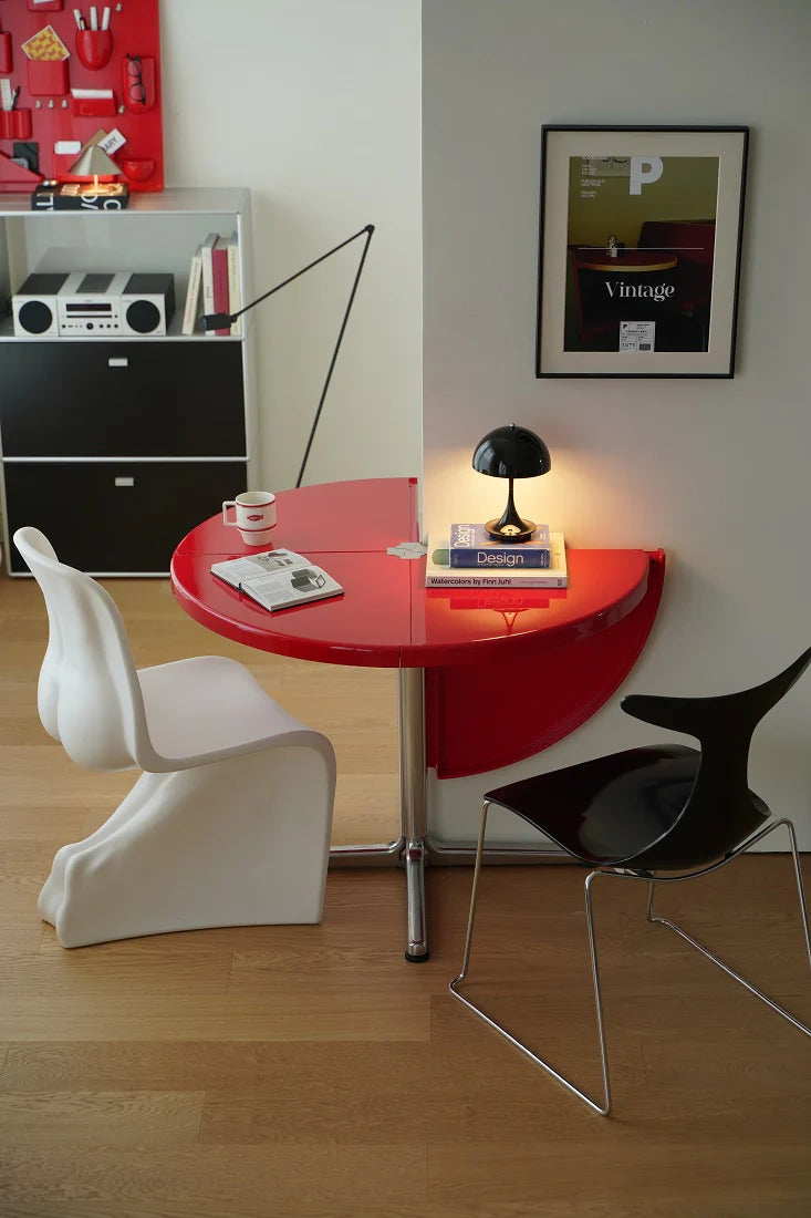 Modern interior with a red round table, white chair, and black chair against a wall with a framed picture.