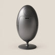 A matte black egg-shaped electronic device on a matching circular stand, photographed against a solid light beige background.