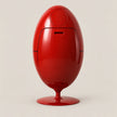 A glossy red egg-shaped container or dispenser with a pedestal base, photographed against a plain light beige studio background.