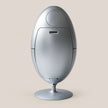 A sleek, metallic silver egg-shaped electronic device with a circular top panel and a round pedestal base, set against a solid light beige background.