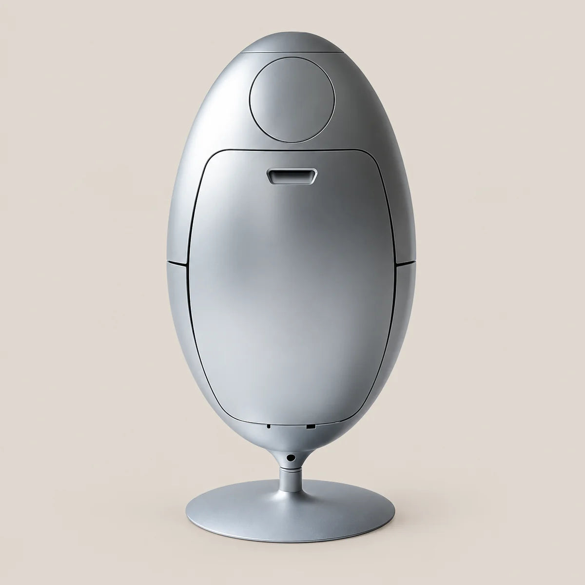 A sleek, metallic silver egg-shaped electronic device with a circular top panel and a round pedestal base, set against a solid light beige background.