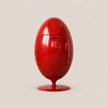 A glossy red egg-shaped electronic device on a matching red pedestal base, photographed against a plain light beige studio background.