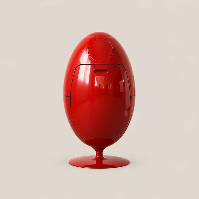A glossy red egg-shaped electronic device on a matching red pedestal base, photographed against a plain light beige studio background.