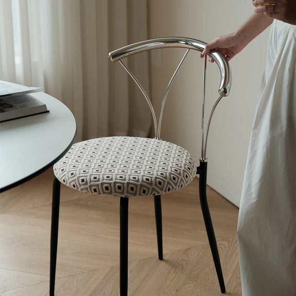 Chair with patterned cushion being held by a person in a room with a table and curtains.